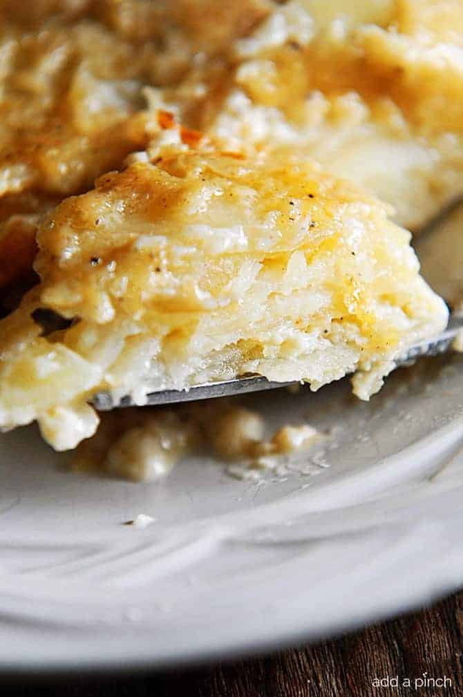 Closeup thin slices of potatoes in a creamy sauce served on a white plate.